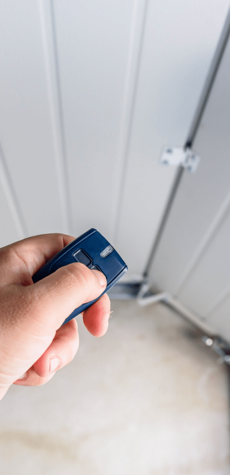 Hand holding a garage door remote beside a white door panel