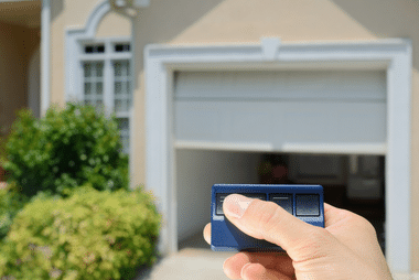 Hand holding a remote in front of a partially open roller door