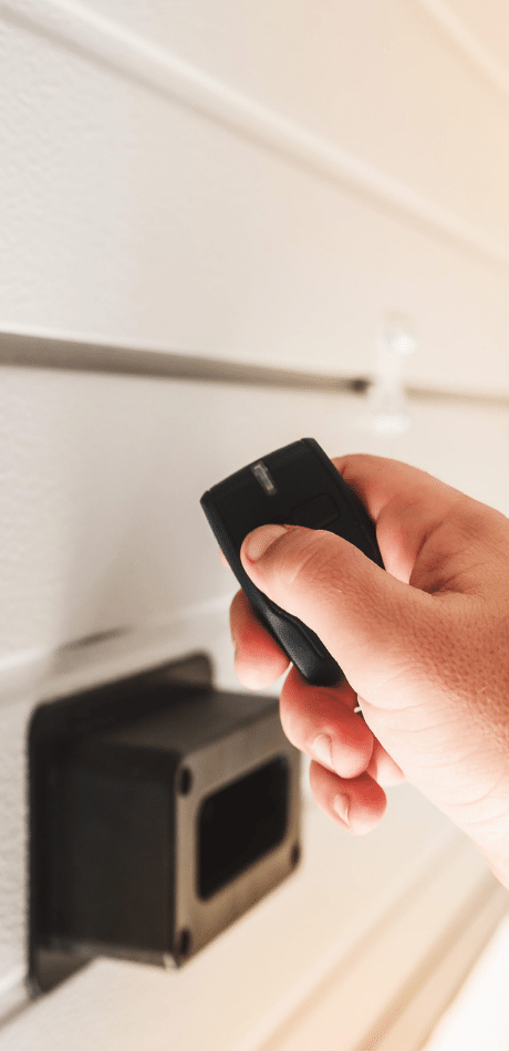 Hand holding a remote near a photoelectric safety sensor on the door track