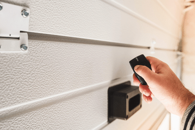 Hand holding a remote beside a receiver unit on the door track