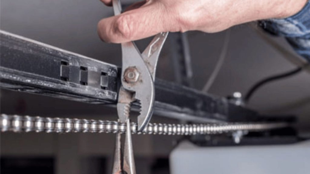 Close-up of pliers adjusting a garage door opener's drive chain on the overhead rail